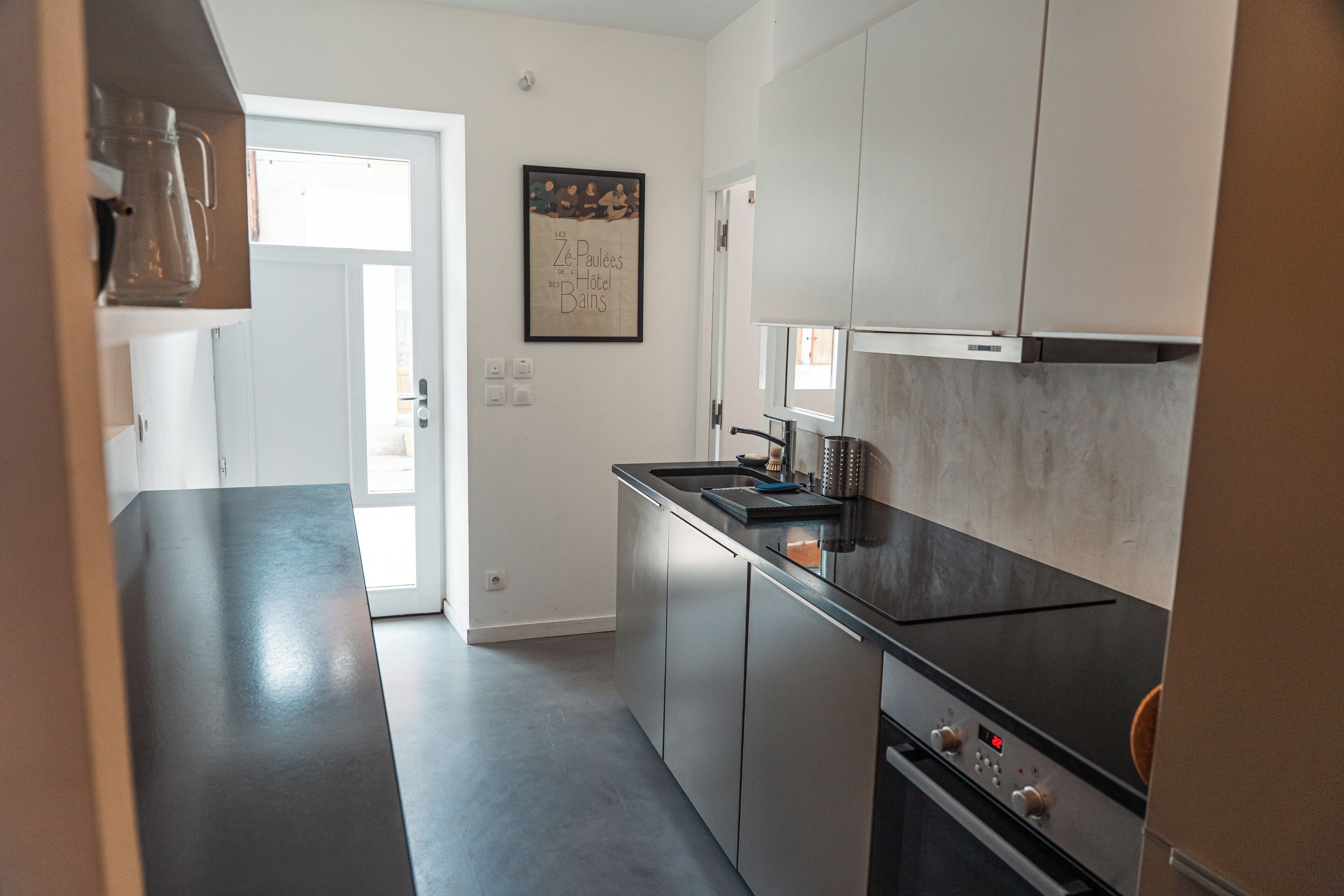 Een moderne keuken met roestvrijstalen apparatuur, een zwart aanrecht en een deur naar een lichte ruimte.