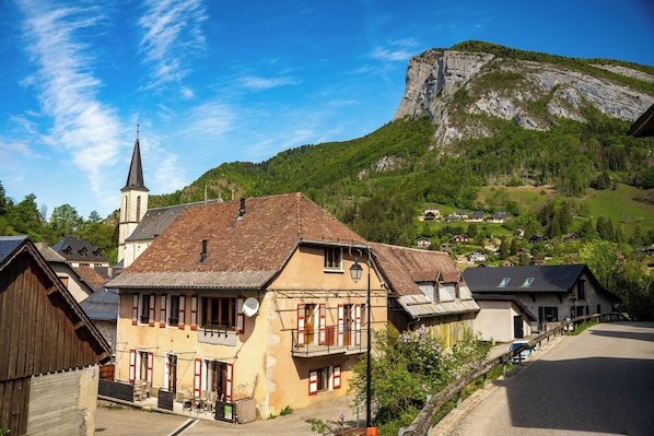 A traditional European village with a church, a prominent mountain in the background, and a paved street.