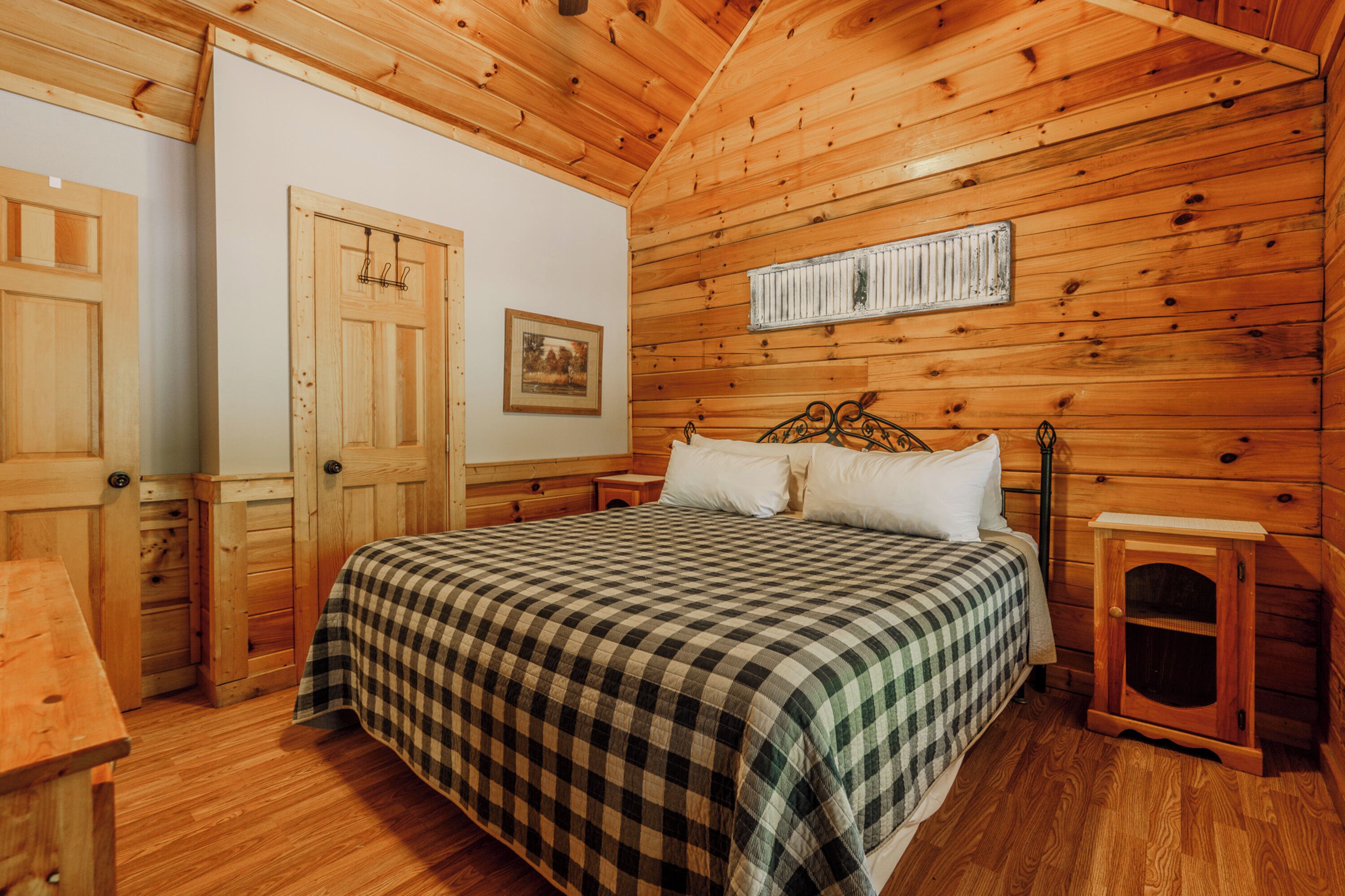 A wooden cabin bedroom with a bed, a dresser, and a small cabinet.