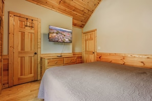 Ein Schlafzimmer mit Holzwänden und -decke, einem Bett mit gemustertem Überwurf, einem an der Wand befestigten Fernseher und Holztüren.