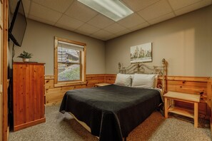 A bedroom with a bed, wooden headboard, a window, a television, and a small table. - Porchside Pines (Pigeon Forge)