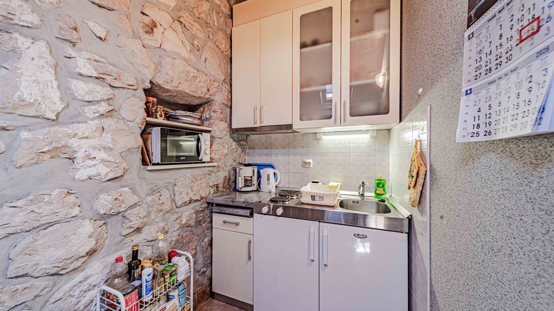 A compact kitchen with stone walls, a built-in oven, a coffee machine, and a refrigerator.
