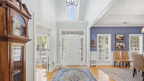 Un couloir avec un plancher en bois, un tapis à motifs bleus, une porte blanche et une horloge.