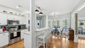 Une cuisine moderne avec des meubles blancs, des appareils en acier inoxydable et un coin bar doté de chaises blanches.