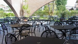 An outdoor patio area with tables and chairs, a brick arch structure, and greenery in the background. - Affittacamere e Ristorante Ariete (Ponsacco)