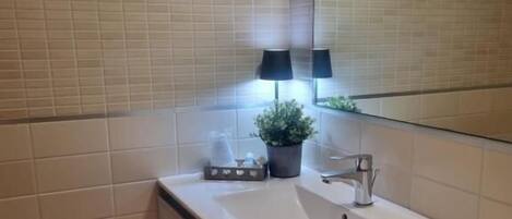 A bathroom with a white sink, a mirror, a potted plant, and a black lamp.