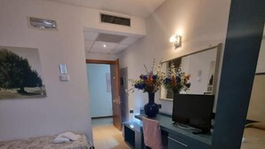 A hotel room with a bed, a desk with a computer, a TV, and a bathroom visible in the background. - Affittacamere e Ristorante Ariete (Ponsacco)