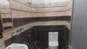 Ein Badezimmer mit Waschbecken, Toilette und einem blauen Eimer auf einem Hocker.