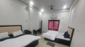 Ein Hotelzimmer mit zwei Betten, einem Deckenventilator, einem Fenster mit roten Vorhängen und einem kleinen Tisch mit St ühlen.
