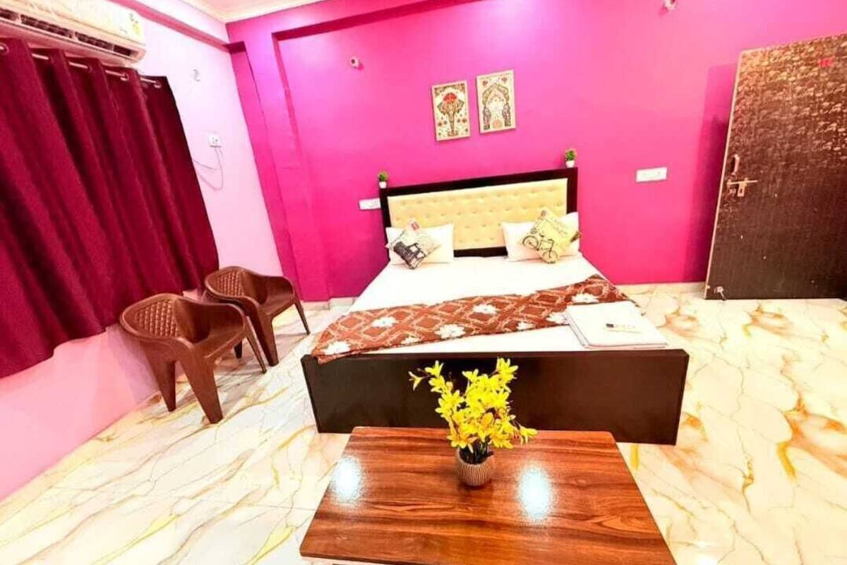 Une chambre à coucher avec un lit, une table de chevet ornée de fleurs, une chaise et un mur rose.