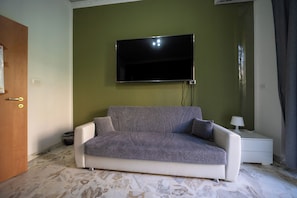 A living room with a sofa, a flat-screen TV mounted on the wall, a nightstand with a lamp, and a door. - Mi Casa Tu Casa (villa Bellini) (Catania)