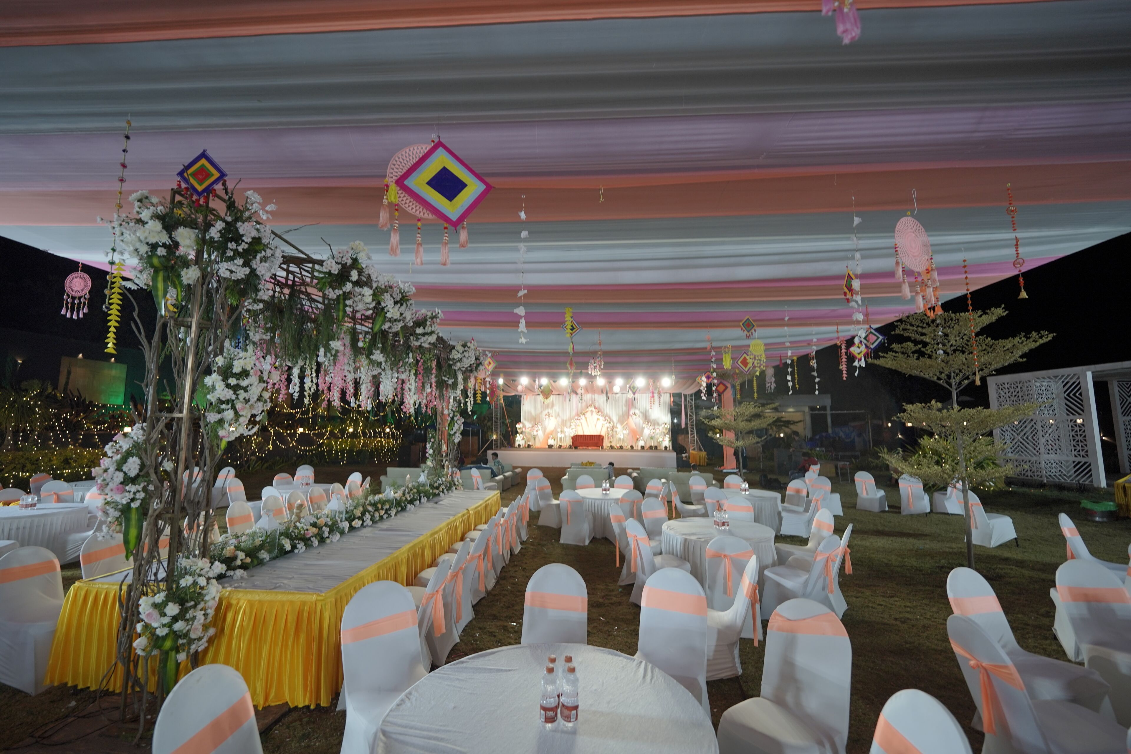 Een evenementenlocatie buiten met ronde tafels, witte stoelen en een podium.