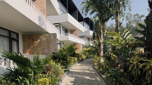 A multi-story hotel with balconies, a paved walkway, and lush greenery.