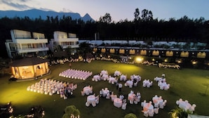 An outdoor event with round tables and chairs, surrounded by buildings and a mountainous backdrop.