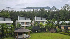 A hotel with multiple white buildings, a central gazebo, lush greenery, and mountains in the background.