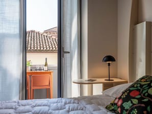 Ein Hotelzimmer mit Bett, Schreibtisch mit Stuhl, Lampe und Blick auf ein Gebäude mit Ziegeldach.