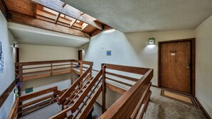 Uma escadaria de madeira com vários níveis, um claraboia, uma porta com número e uma pequena luminária na parede.