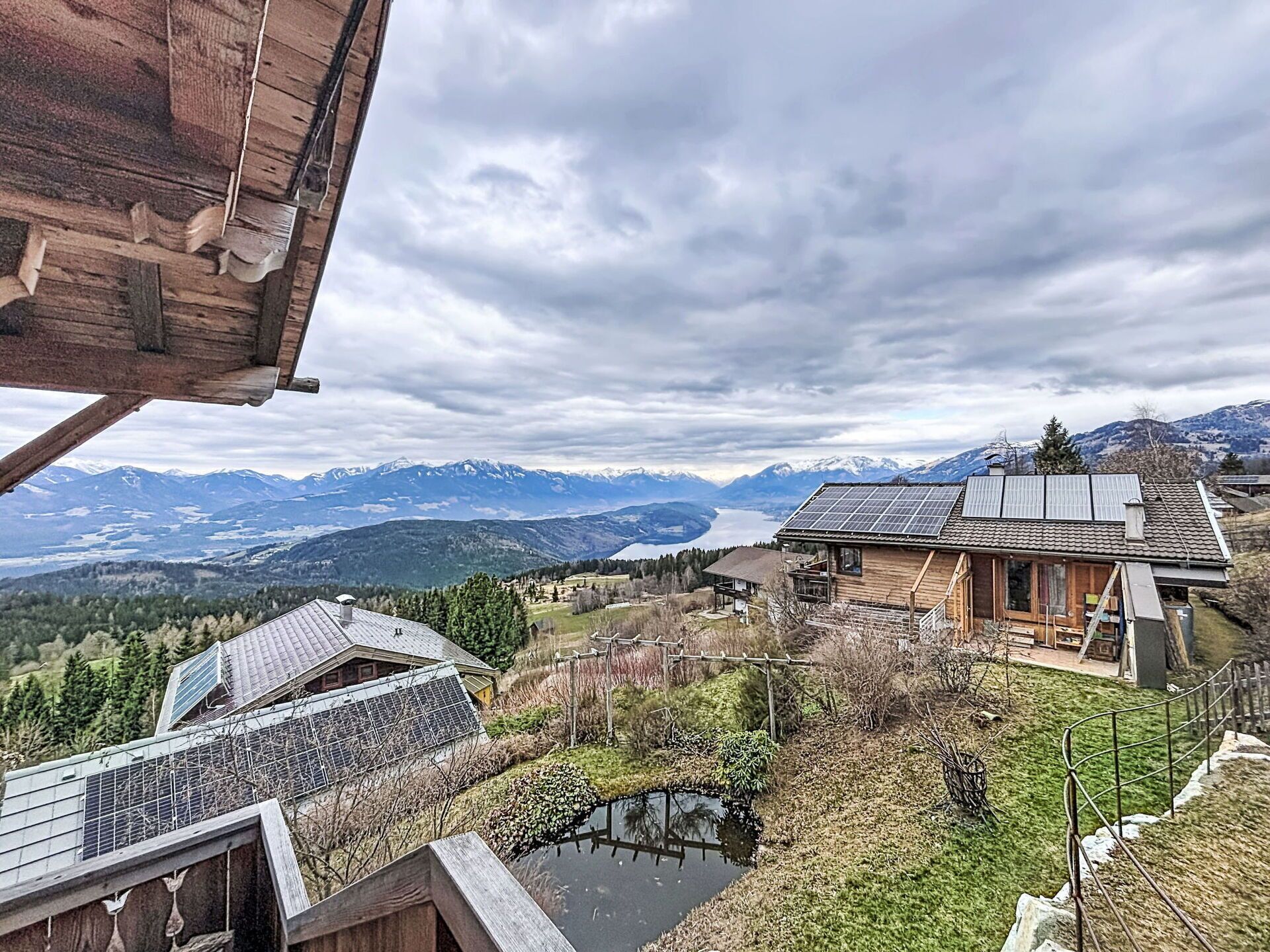 Une cabane en bois équipée de panneaux solaires, avec un étang et un paysage montagneux en arrière-plan.