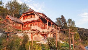 Eine Holzhütte mit Balkon, umgeben von Grün und einem Bergpanorama.