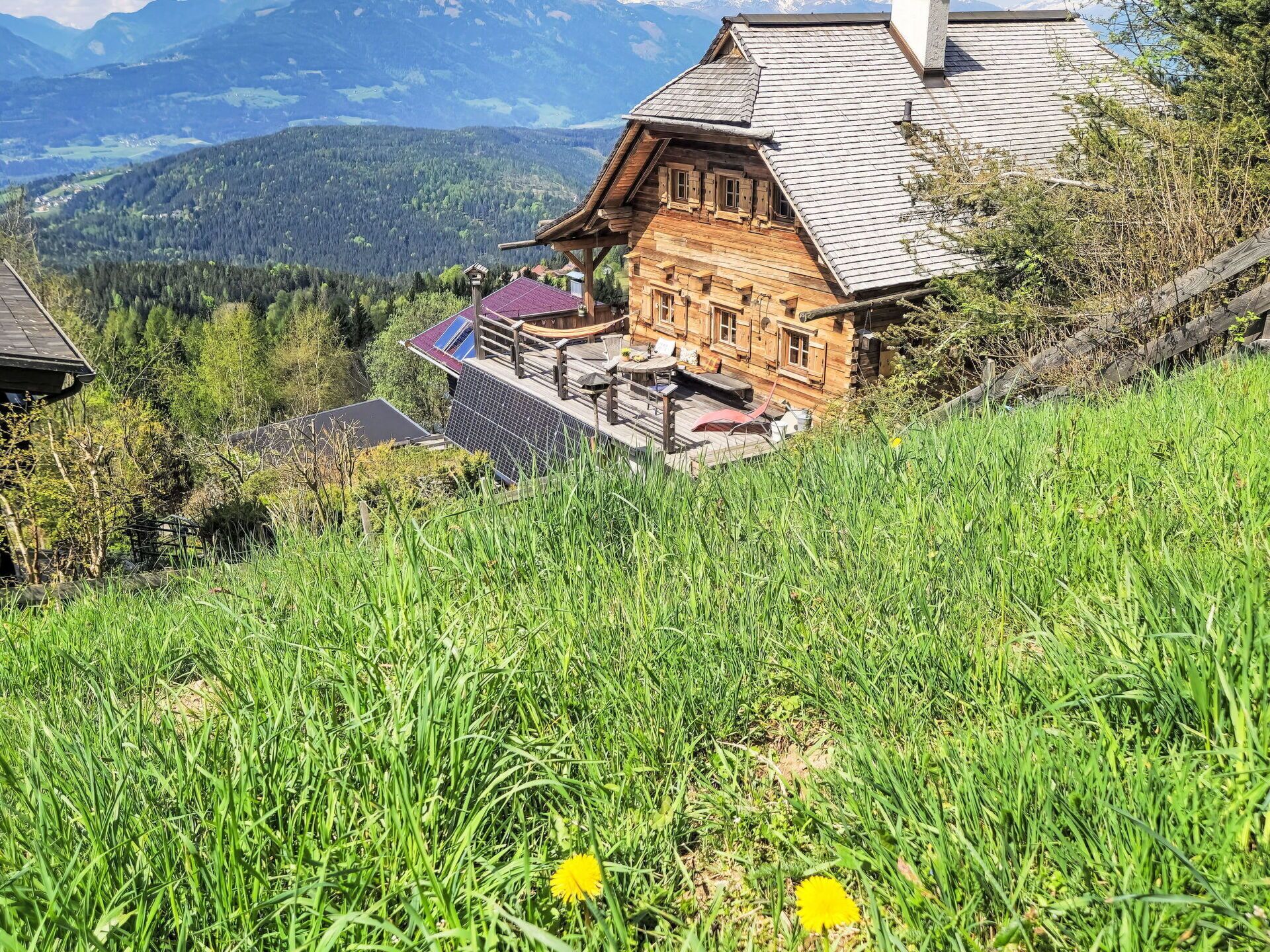 Un chalet en bois doté d’un toit à pente, d’une terrasse avec mobilier d’extérieur et offrant une vue sur les montagnes environnantes.