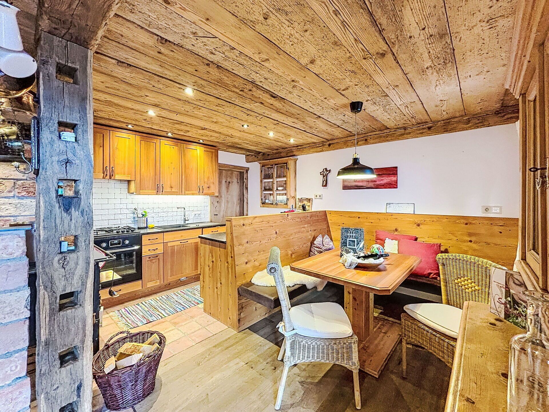 A rustic kitchen with wooden cabinets, a dining table with chairs, and a bench.