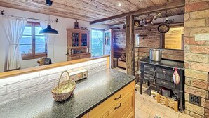 Eine rustikale Küche mit Steinwand, Holzbalkendecke und einem großen Fenster mit Vorhängen.