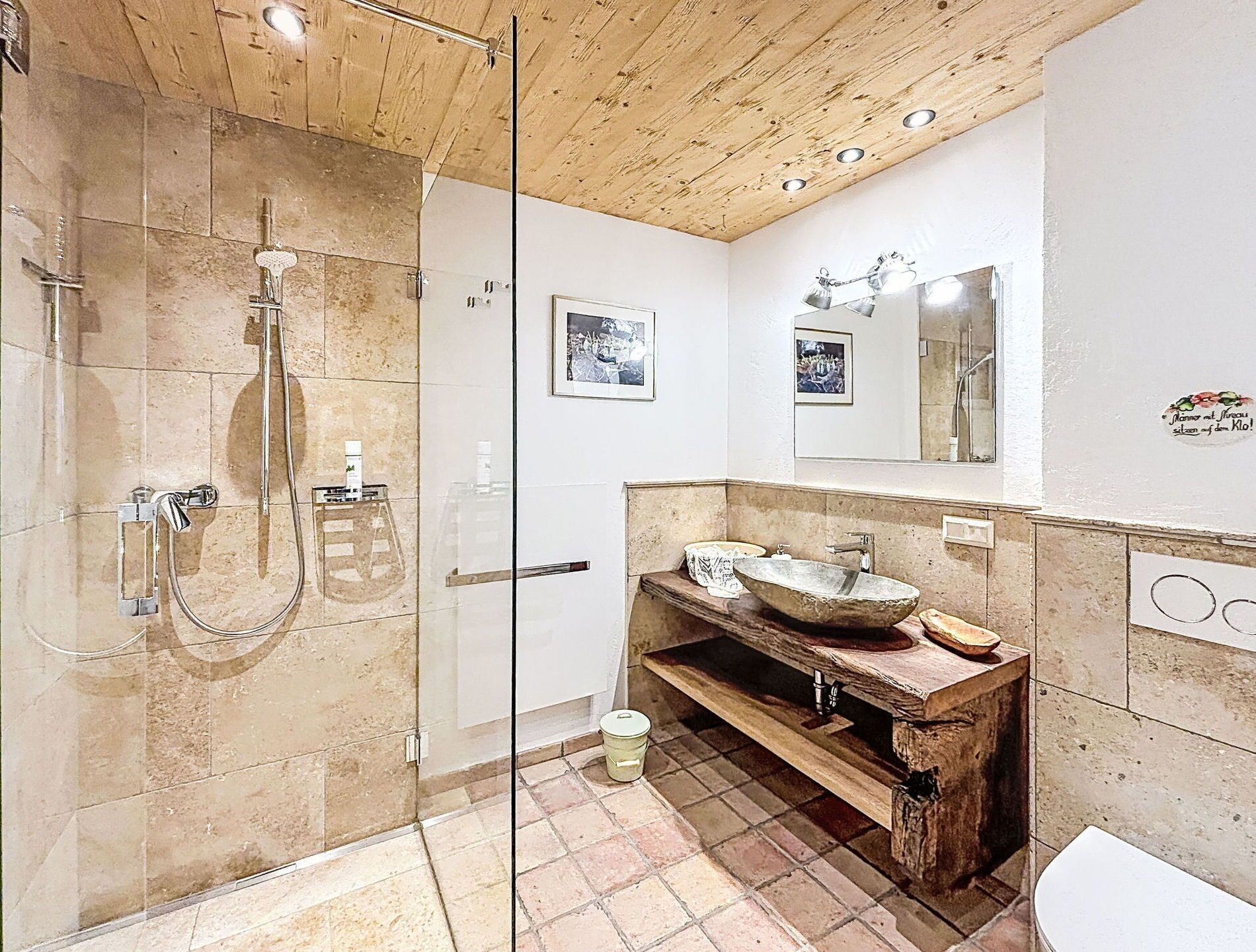 A bathroom with a glass shower enclosure, a wooden vanity, a large mirror, and a tiled floor.