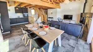 Ein Essbereich mit Holztisch und -stühlen, im Hintergrund eine Küche und eine Treppe, die zu einer oberen Ebene führt.