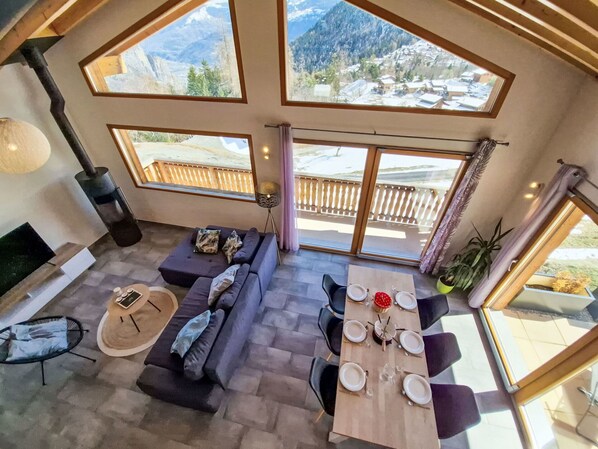 A modern interior with a dining area, sofas, and large windows offering mountain views.