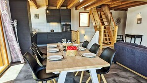 Ein Essbereich mit einem Holztisch, gedeckt für sechs Personen, schwarzen Stühlen, einer Küche im Hintergrund und einer Treppe.