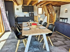 Ein Essbereich mit einem Holztisch, gedeckt für sechs Personen, schwarzen Stühlen, einer Küche im Hintergrund und einer Treppe.