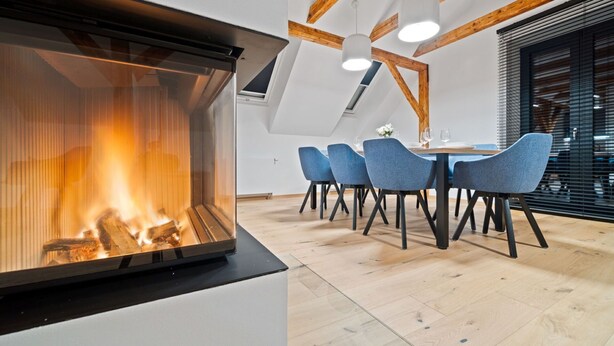 A modern dining area with a fireplace, wooden beams, and blue chairs.
