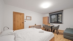 A bedroom with a bed, a desk, chairs, a window with blinds, and a small sofa.