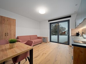 A modern interior with a wooden dining table, a sofa, a kitchen area, and a sliding glass door leading to a snowy outdoor area.