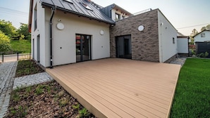 A modern two-story house with a flat roof, a balcony, and a paved deck.