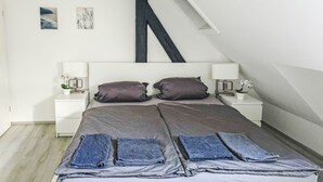 Ein Schlafzimmer mit einem Bett, zwei Nachttischen, einer Lampe, einer Pflanze und Bildern an der Wand.