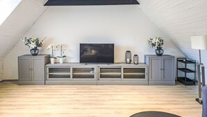 Ein modernes Loft mit schrägem Dach, integriertem Fernsehschrank und Zimmerpflanzen.
