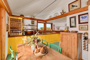 Una cocina con armarios amarillos, una mesa de madera con un florero y pan, y diversos utensilios de cocina.