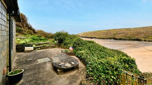 A courtyard with a stone bench, a potted plant, and a view of a beach. - The Cuddy (Porthcothan Bay)