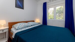 Een slaapkamer met een bed, nachtkastje, lamp, raam met gordijnen, en een ingelijst schilderij aan de muur.