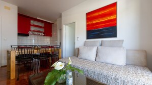 Een woonkamer met een bank, een eethoek met stoelen, een keuken met rode kasten, en een groot abstract schilderij.