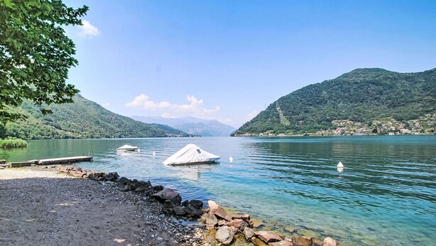 Un lago con barche, un molo e una riva rocciosa.