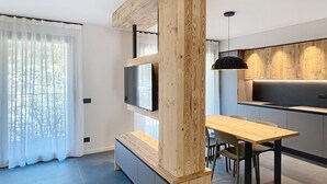 Une cuisine moderne avec un mur d’accent en bois, un coin repas avec une table et des chaises, et un téléviseur fixé au mur.