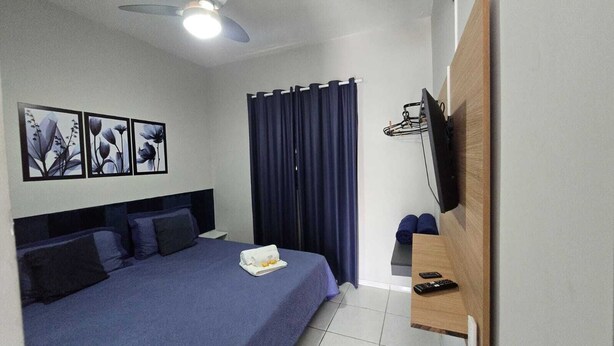 Une chambre d’hôtel équipée d’un lit, d’un téléviseur à écran plat fixé au mur, d’un ventilateur de plafond et d’une fenêtre avec des rideaux.