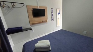 Une chambre à coucher avec un lit, un téléviseur fixé au mur, une serviette et une étagère.