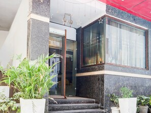 Entrada de hotel con puerta de cristal, escalones que la conducen y plantas en macetas.