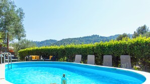 En pool med solstolar, ett brickbord med drycker och utsikt över kullar.