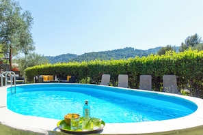 A swimming pool with lounge chairs, a tray with drinks, and a view of hills. - Group villa with private pool (Imperia)