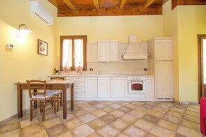 A kitchen with white cabinets, a wooden dining table with chairs, a tiled floor, and a red towel hanging on the right. - Group villa with private pool (Imperia)