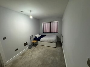 Une chambre à coucher comprenant un lit, une chaise, un bureau, une fenêtre avec des stores et un luminaire au plafond.